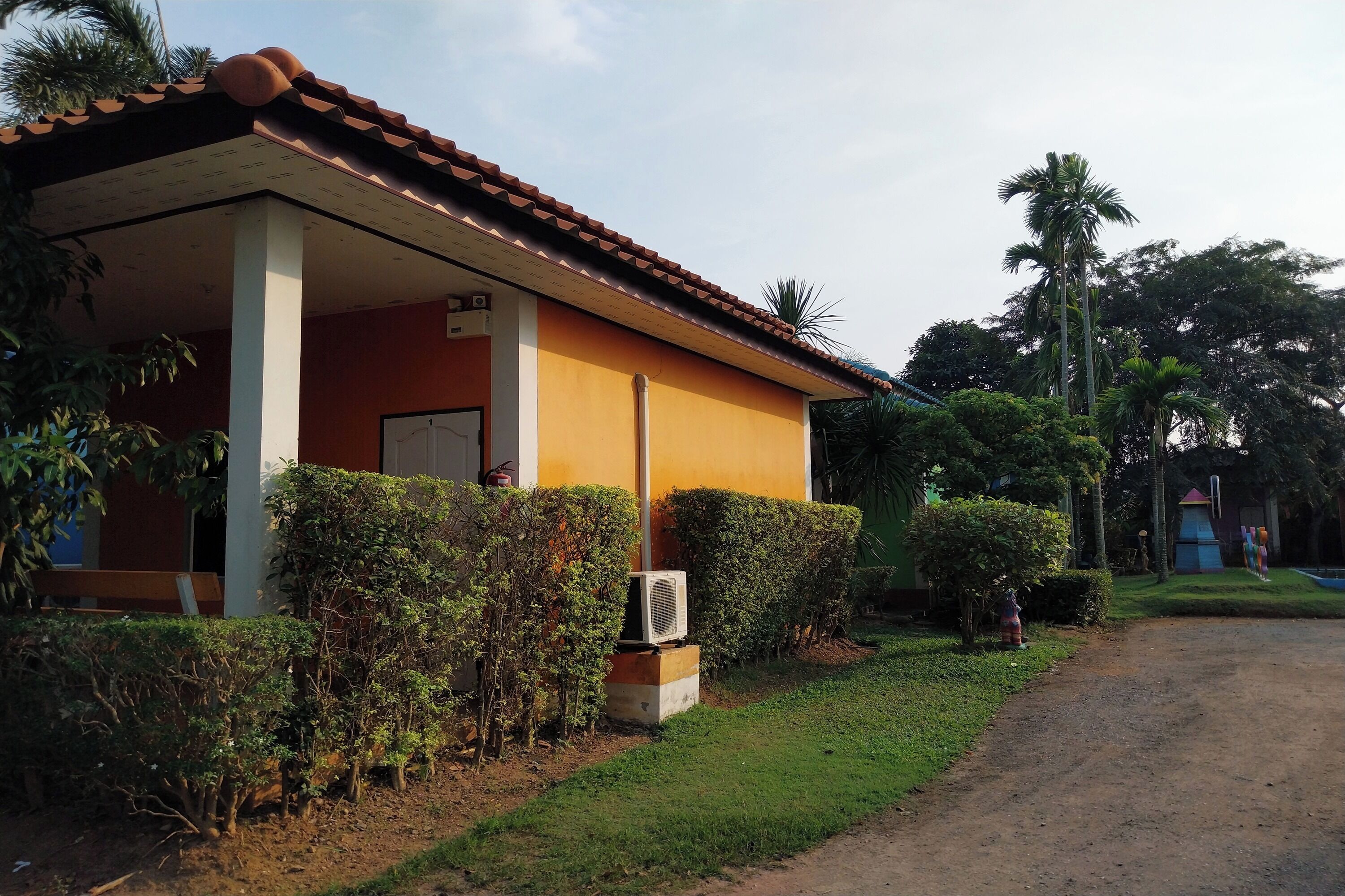 A single-story building with a tiled roof, surrounded by well-maintained hedges and palm trees.