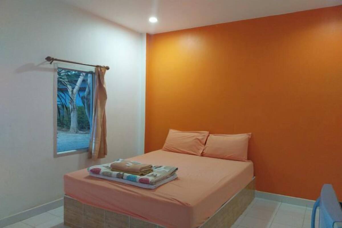 A bedroom with a bed, a window with a view of trees, and an orange wall.
