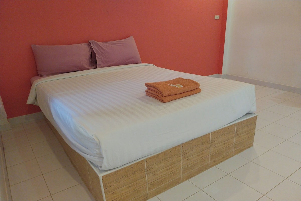 Cama bem arrumada com toalha dobrada, cabeceira de madeira e parede lisa em quarto de hotel.