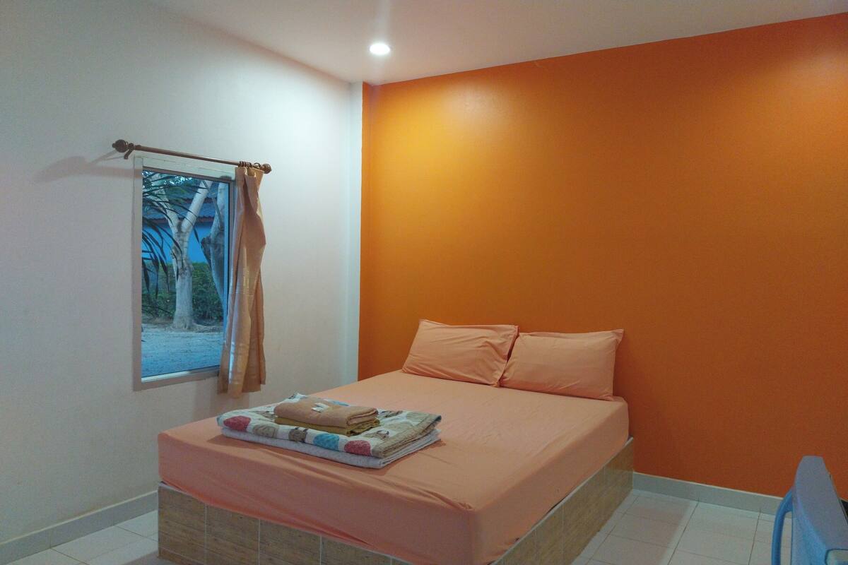Quarto com cama, paredes laranja, janela com cortinas e vista para árvores.