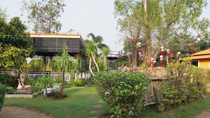 A garden with a statue, a building with a sloped roof, and a bamboo fence. - Review Resort (Sattahip)