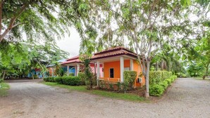 A row of colorful cottages with a gravel path leading to them, surrounded by lush greenery. - Review Resort (Sattahip)