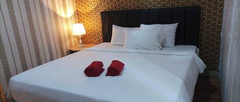 A neatly made bed with white linens, two rolled red towels, and a black headboard.