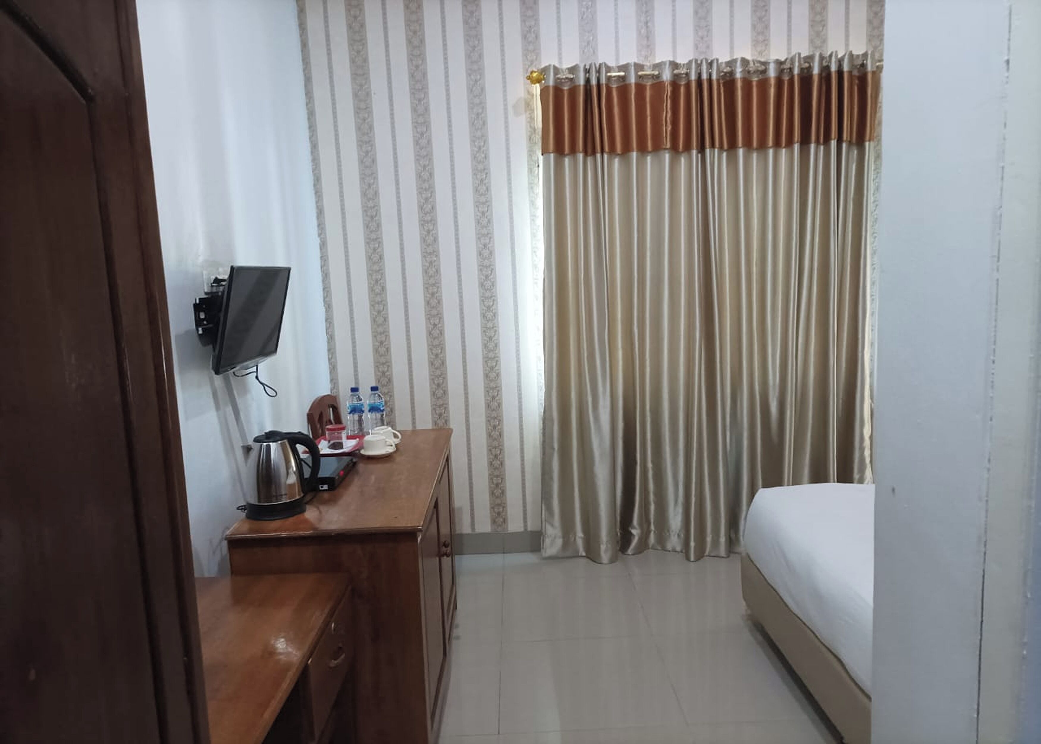 Ein Hotelzimmer mit Bett, Schreibtisch mit Wasserkocher, Fernseher und einem fenster mit Vorhängen.