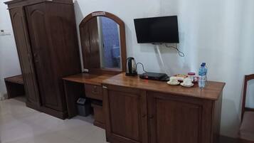 A wooden cabinet with a mirror, a television mounted on the wall, a kettle, and a few items on the counter.
