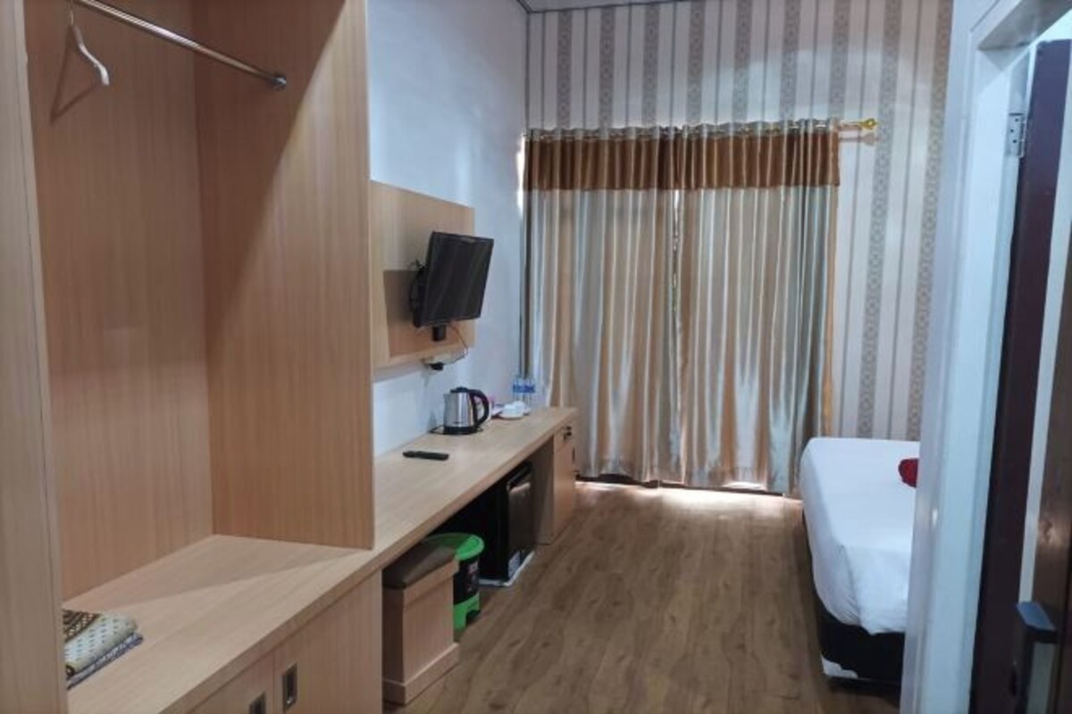 A hotel room with a wooden wardrobe, a TV mounted on the wall, a bed with a white bedspread, and a curtain with a striped pattern.