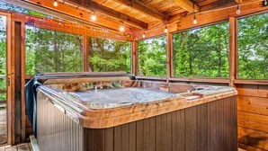 Een houten jacuzzi met een houten terras, grote ramen en lichtslingers.