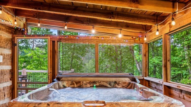 Een hottub in een houten hut met grote ramen en lichtslingers.