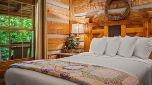 Een slaapkamer in een blokhut met een bed, een raam, een aan de muur bevestigd kerstkransje en een kleine kerstboom.