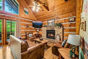 A cozy cabin interior with a stone fireplace, leather furniture, and a television.