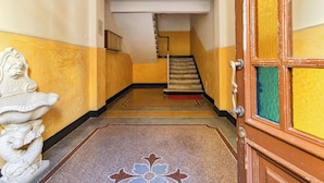 A hallway with a staircase leading to an upper floor, a decorative white sculpture on the left, and a wooden door with a green glass panel on the right. - Central & Cozy Apartment by Wonderful Italy (Genoa)