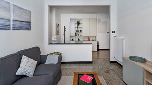 A modern living room with a grey sofa, a coffee table, and a kitchen area in the background. - Central & Cozy Apartment by Wonderful Italy (Genoa)