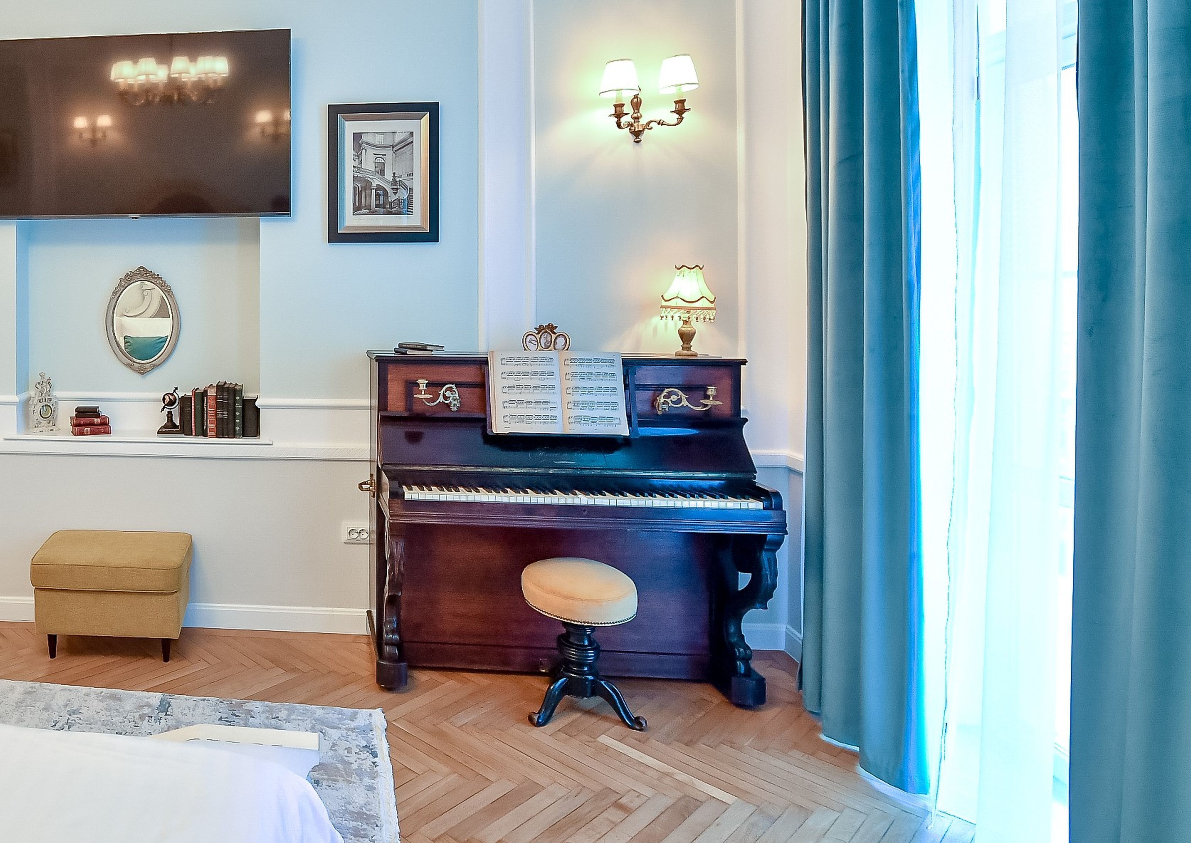 A room with a grand piano, a small stool, a television, wall sconces, and a framed picture.