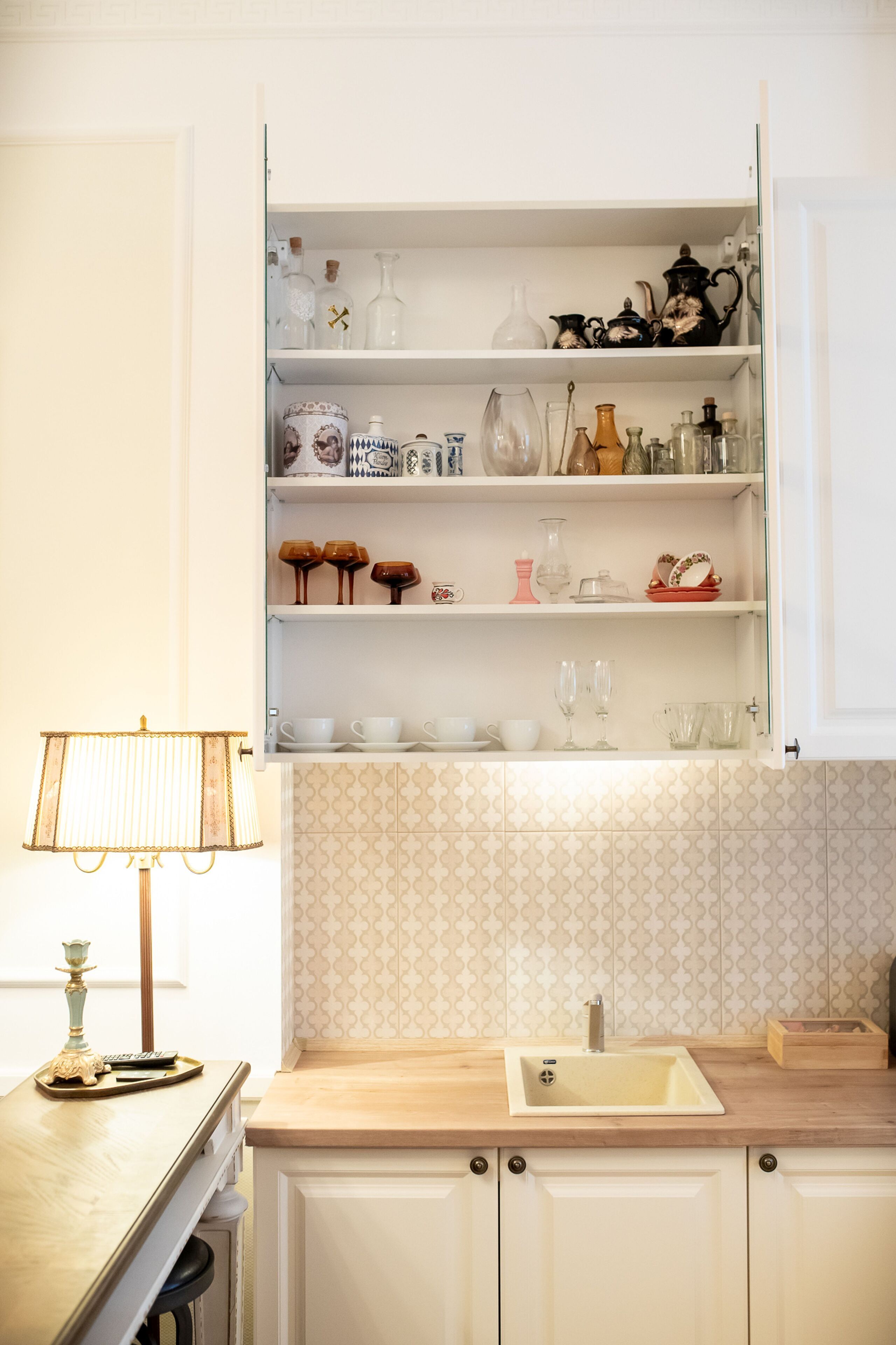 Una cocina con encimera de madera, un lavabo y un armario con cristalería y vajilla.