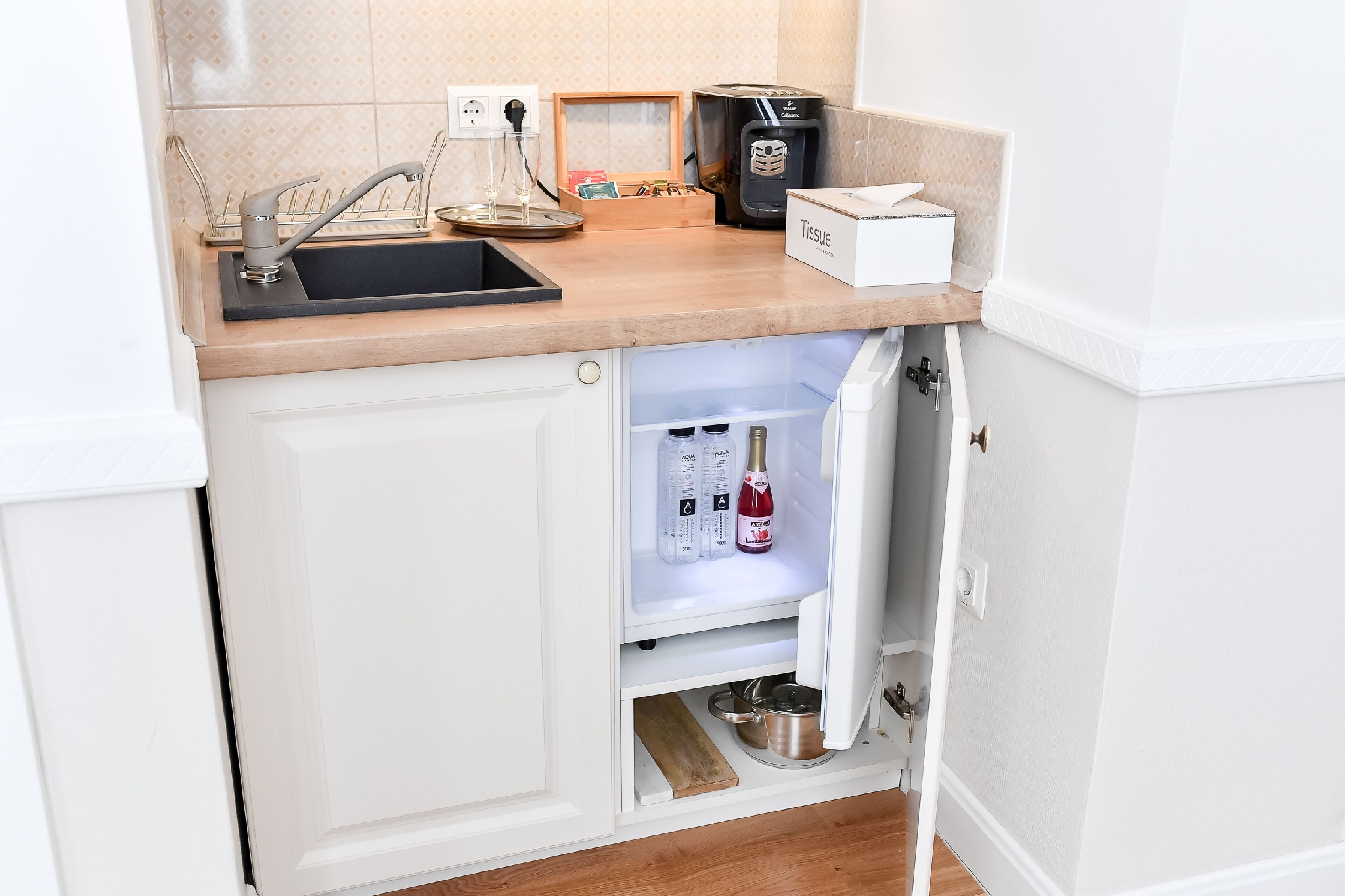 A kitchen with a built-in sink, a coffee maker, a tissue box, and a refrigerator with a drawer containing bottles and a pot.