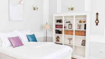 A neatly arranged bedroom with a white bed, a bookshelf, and a wall-mounted clock.
