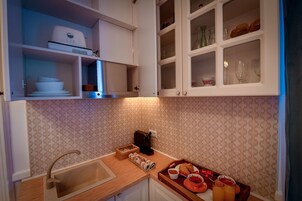 Una cocina con gabinetes blancos, un lavamanos, una cafetera y una bandeja con croissants y jugo de naranja.