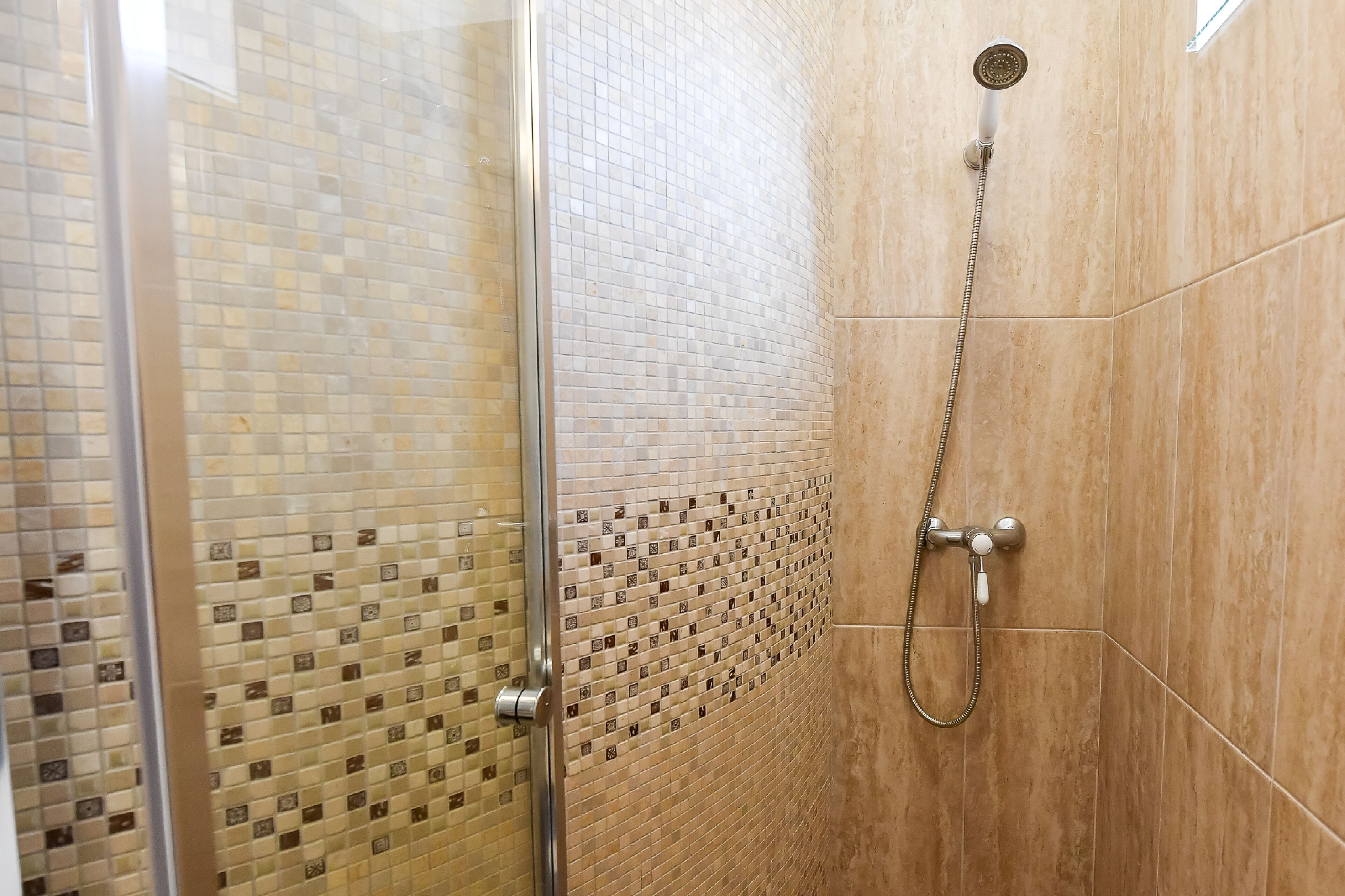 A shower area with a glass door and tiled walls.