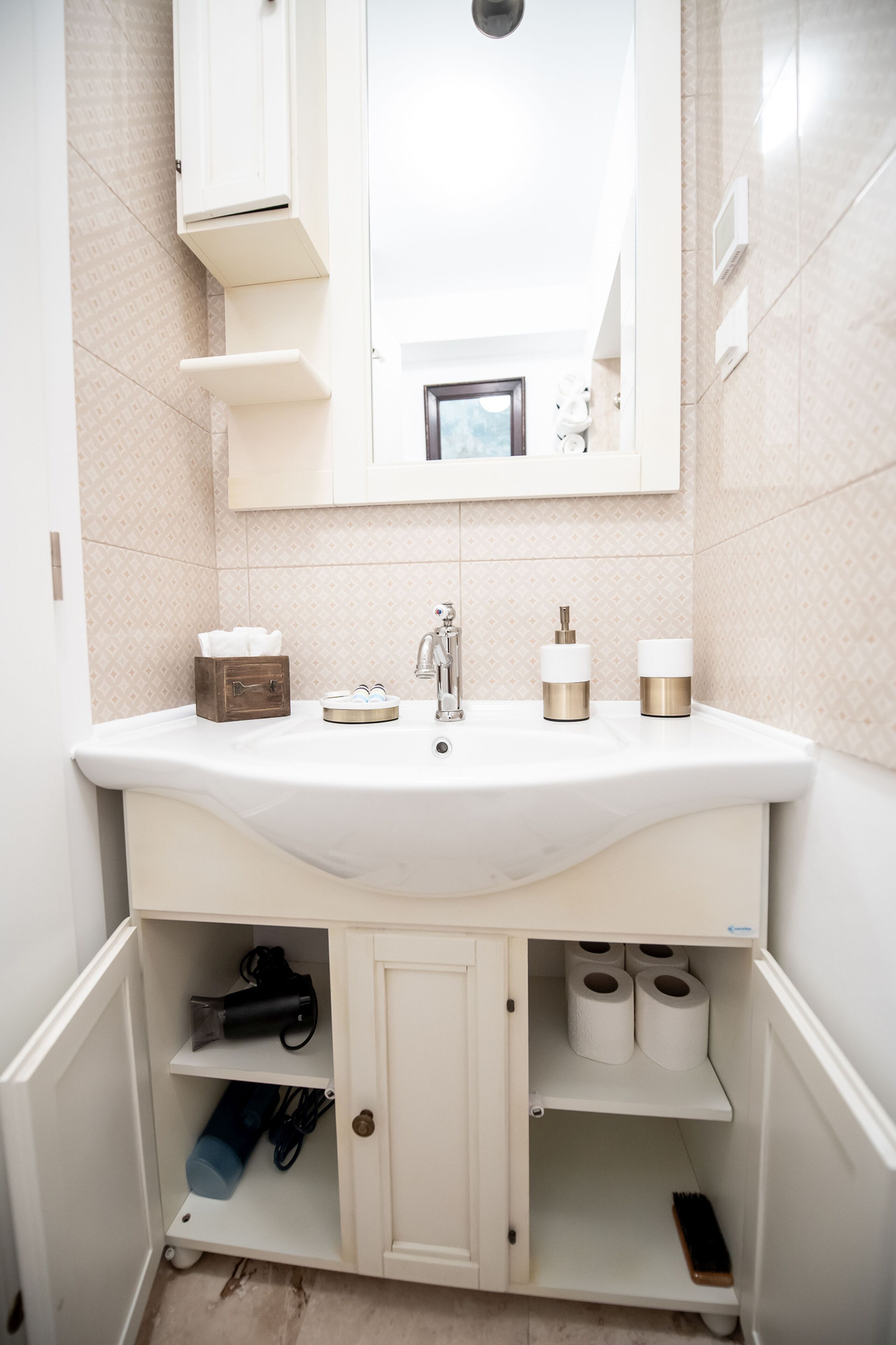 Une salle de bain avec un lavabo blanc, un miroir au-dessus et un meuble en dessous. On y trouve des articles de toilette sur le comptoir et une brosse à dents dans le meuble.