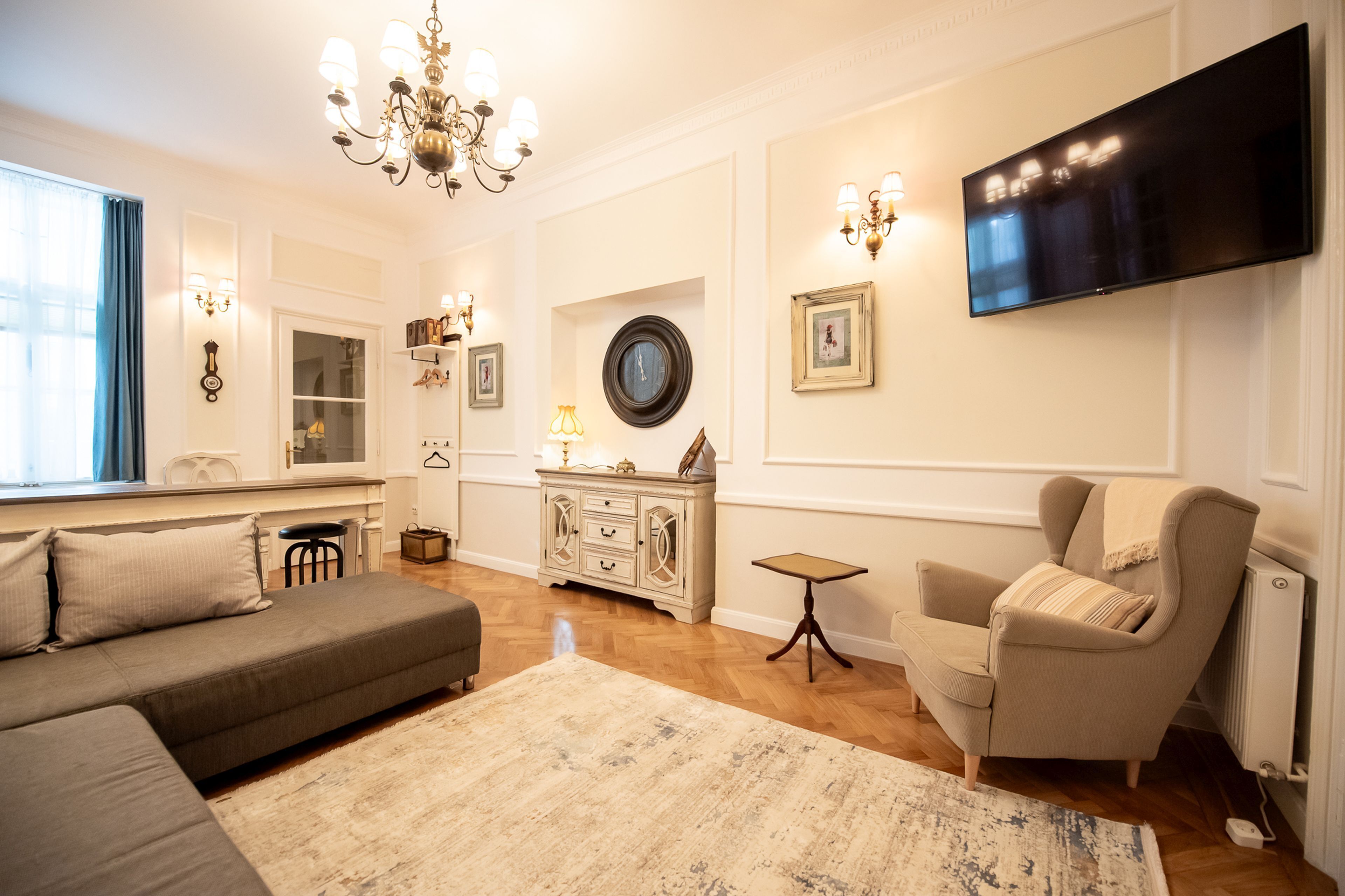 A living room with a sofa, armchair, and a television mounted on the wall.