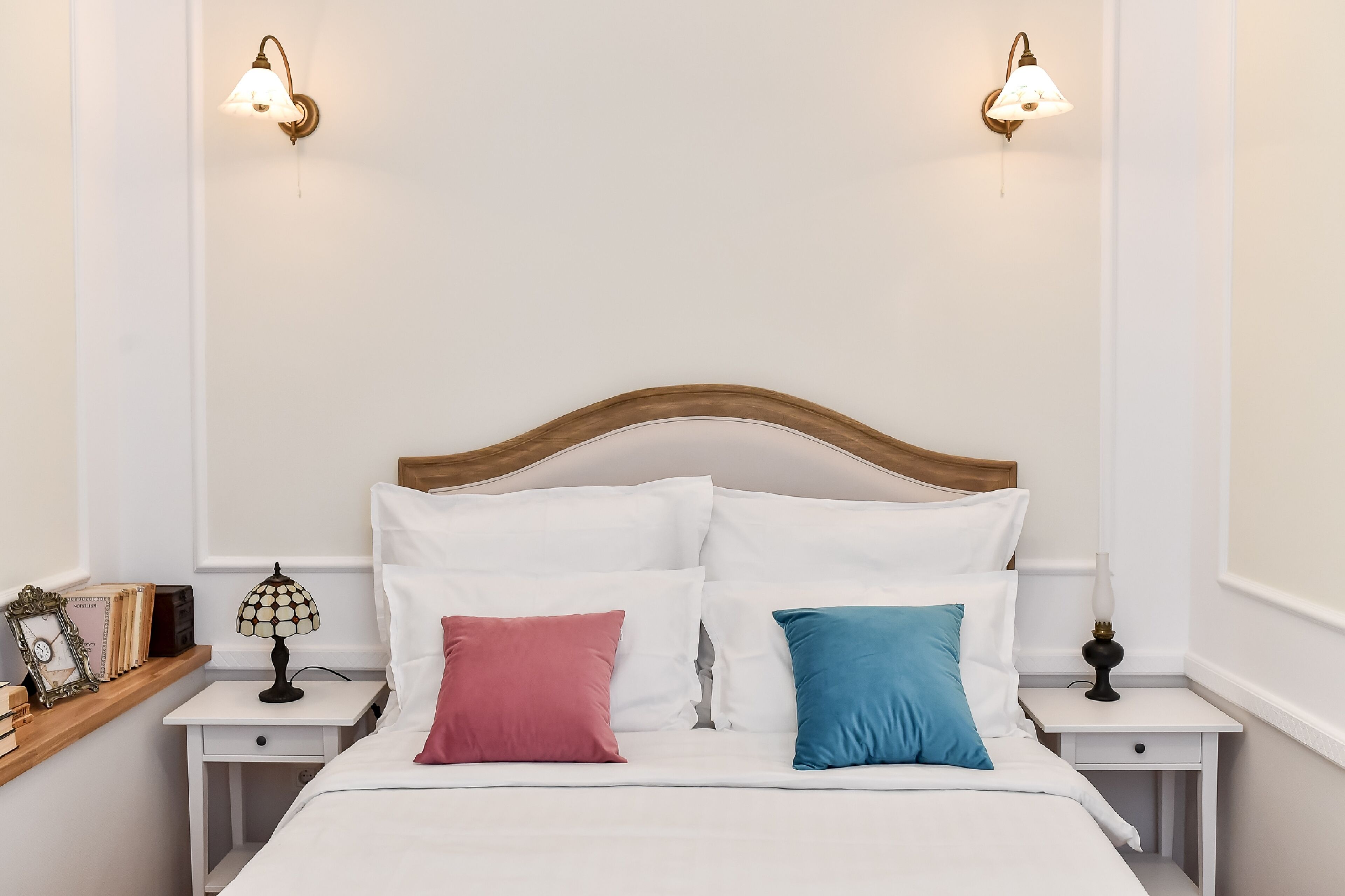 A neatly made bed with white bedding and two pillows, a wooden headboard, and two bedside tables with lamps.