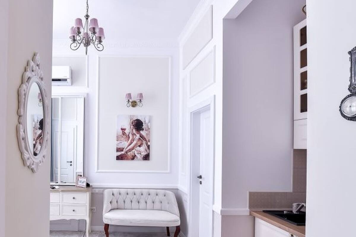 A hallway with a white bench, a mirror, and a chandelier.