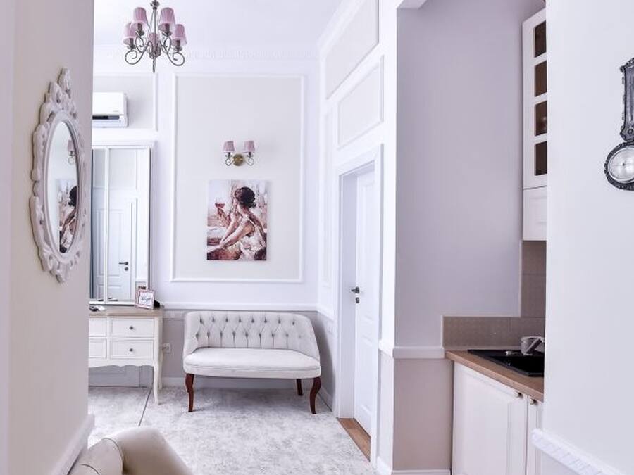 A hallway with a white bench, a mirror, and a chandelier.