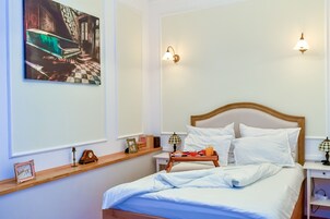 Una cama bien hecha con sábanas blancas, una mesita de noche con lámpara, una bandeja con alimentos para el desayuno y un cuadro sobre la cama.