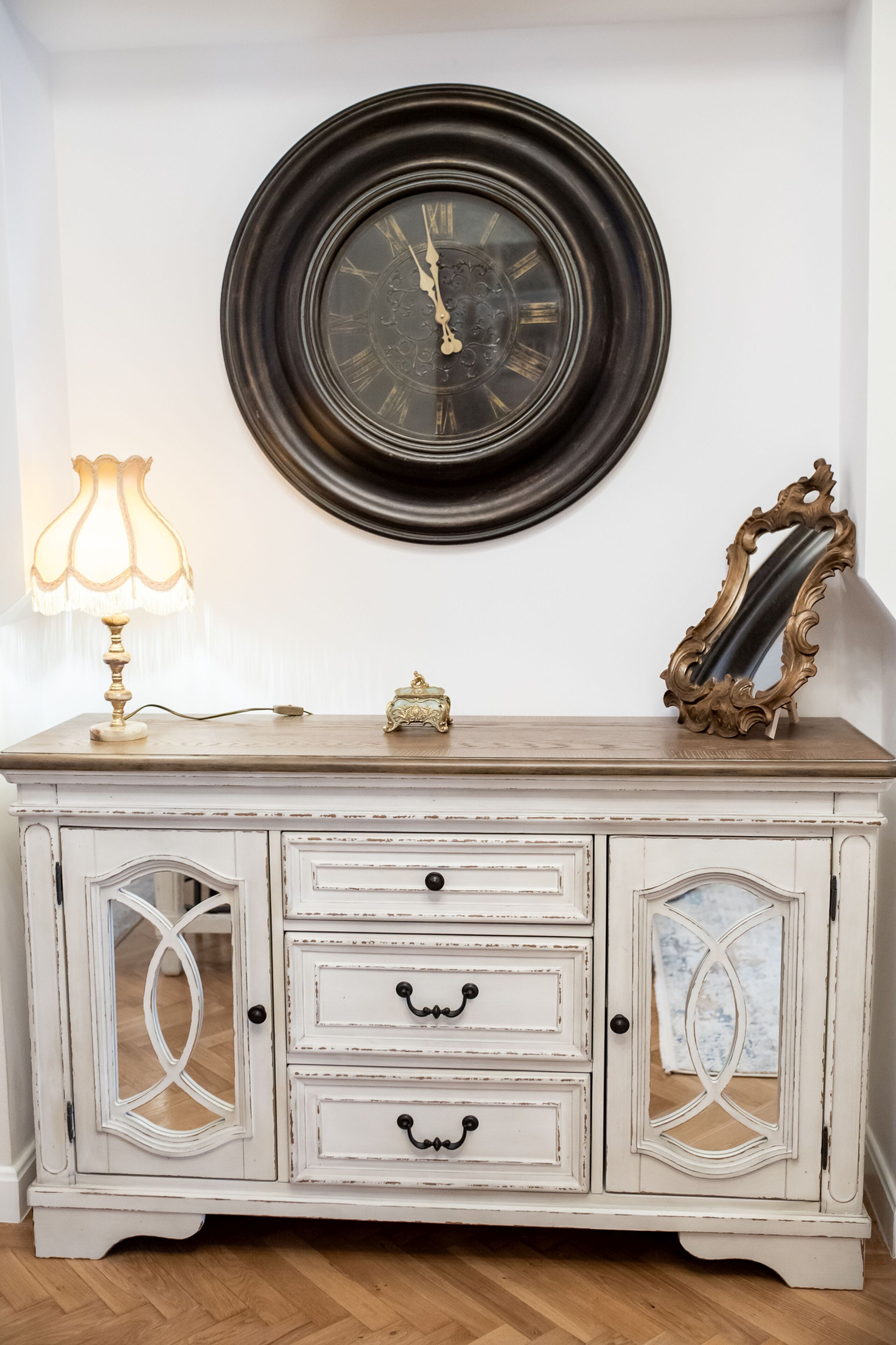 A white cabinet with three drawers, a decorative mirror, and a wall clock.