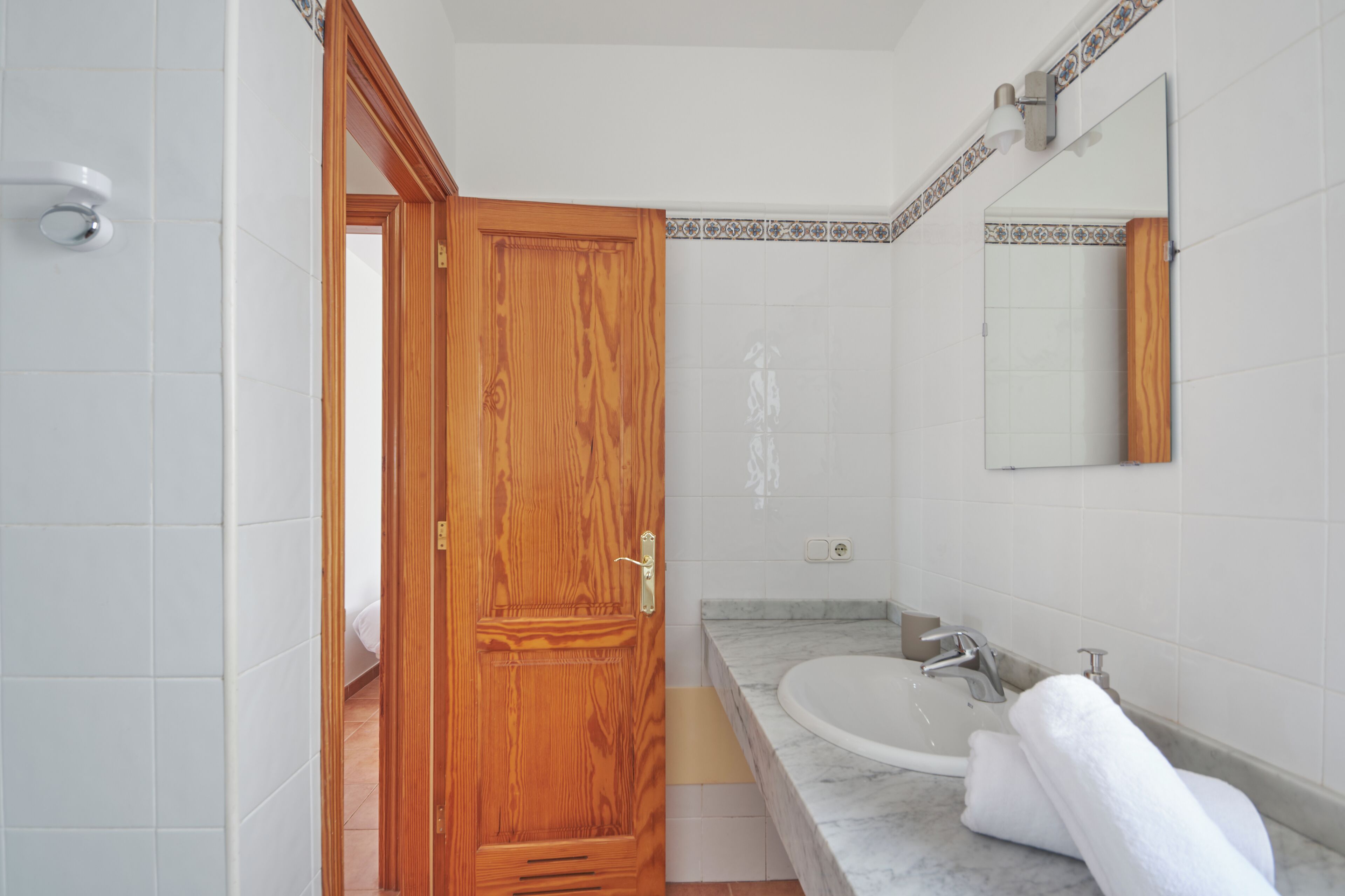 A bathroom with a wooden door, a sink, a mirror, and a towel on the counter.