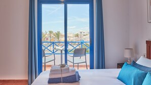 A hotel room with a bed, a nightstand, a lamp, and a view of the outside balcony with chairs and a table. - Casa Maria del Mar 2 Minutes From Supermarkets & 10 Minutes From Marina Rubicón (Playa Blanca)