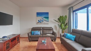 A living room with a brown leather sofa, a wooden coffee table, and a painting of a beach scene. - Casa Maria del Mar 2 Minutes From Supermarkets & 10 Minutes From Marina Rubicón (Playa Blanca)
