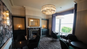 A room with a fireplace, a mirror, and a view of greenery outside. - Cae Mor Hotel (Llandudno)