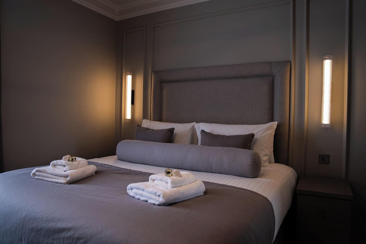 A neatly made bed with two sets of towels, a headboard, and wall-mounted lights.