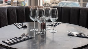 A round table with four wine glasses and cutlery, set against a window with a view of a cityscape and a building. - Cae Mor Hotel (Llandudno)
