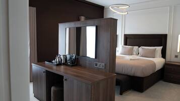 A hotel room with a dark wood desk, a large mirror, a bed with beige bedding, and a modern light fixture.