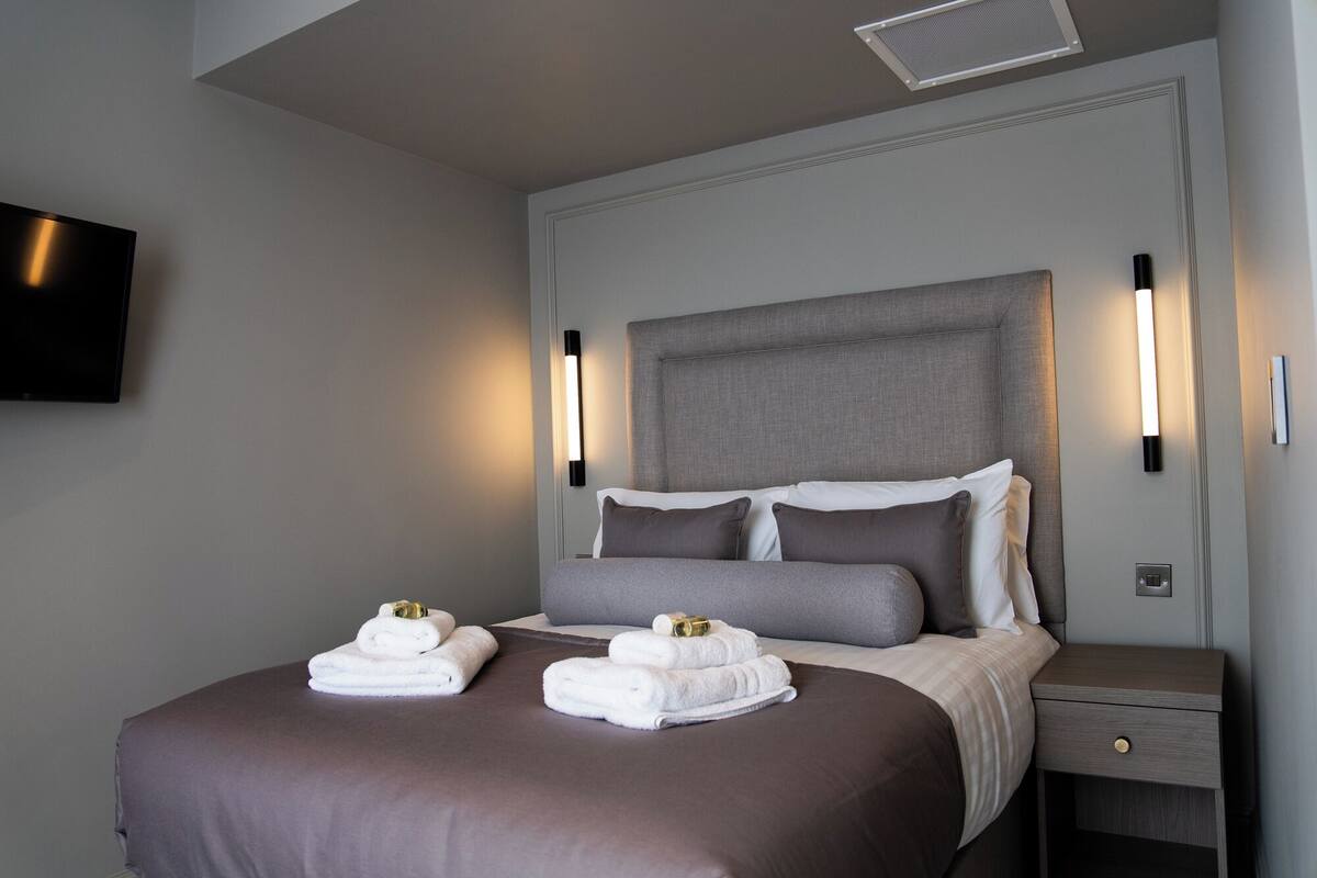 A neatly made bed with gray and white bedding, two bedside tables with lamps, and a flat-screen TV mounted on the wall.