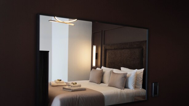 A modern hotel room with a large bed, a bedside table, a wall-mounted light, and a mirror. - Cae Mor Hotel (Llandudno)