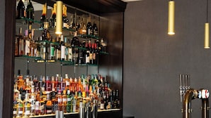 A bar area with a marble countertop, shelves of liquor bottles, and hanging pendant lights. - Cae Mor Hotel (Llandudno)