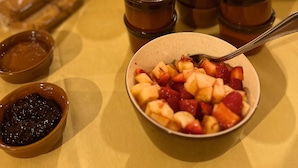A breakfast table with various food items, including a bowl of fruit salad, a pitcher of orange juice, and several small bowls of condiments.