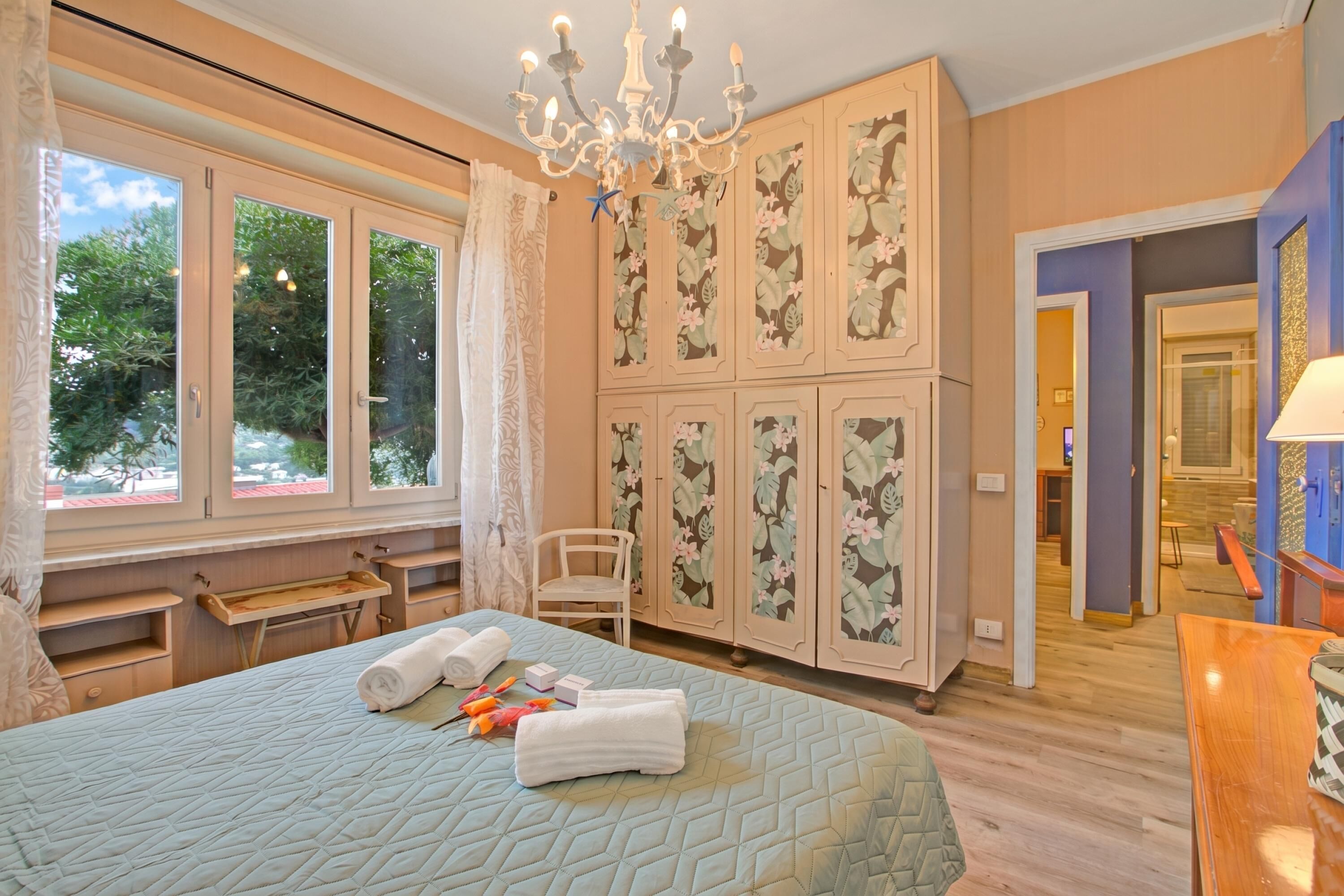 Un dormitorio con cama, una silla, armario y lámpara de araña.