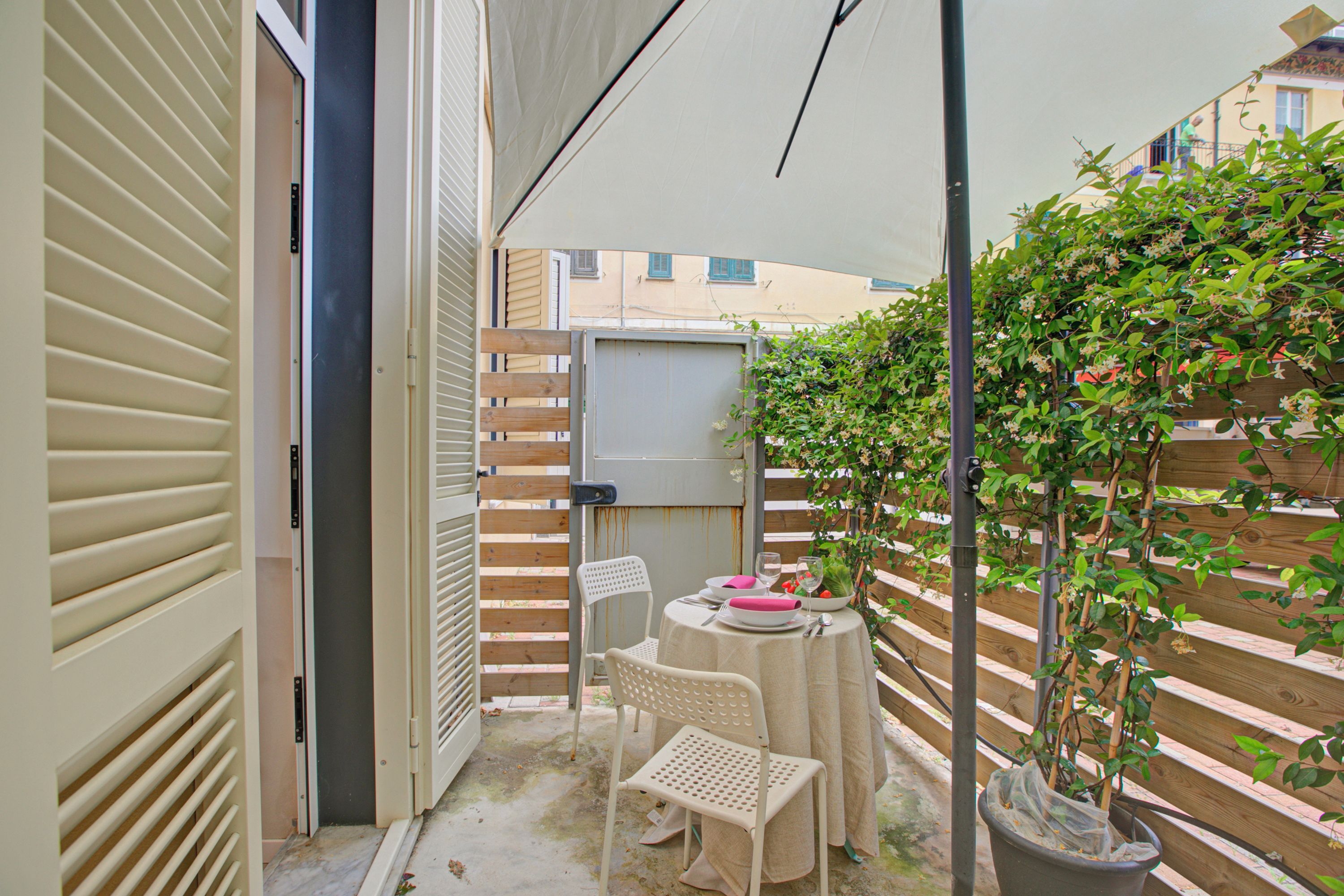 A small outdoor patio with a table and chairs, a potted plant, and a view of the surrounding buildings.