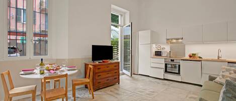 A modern kitchen with white cabinets, a dining area with wooden chairs, and a television on a wooden cabinet.