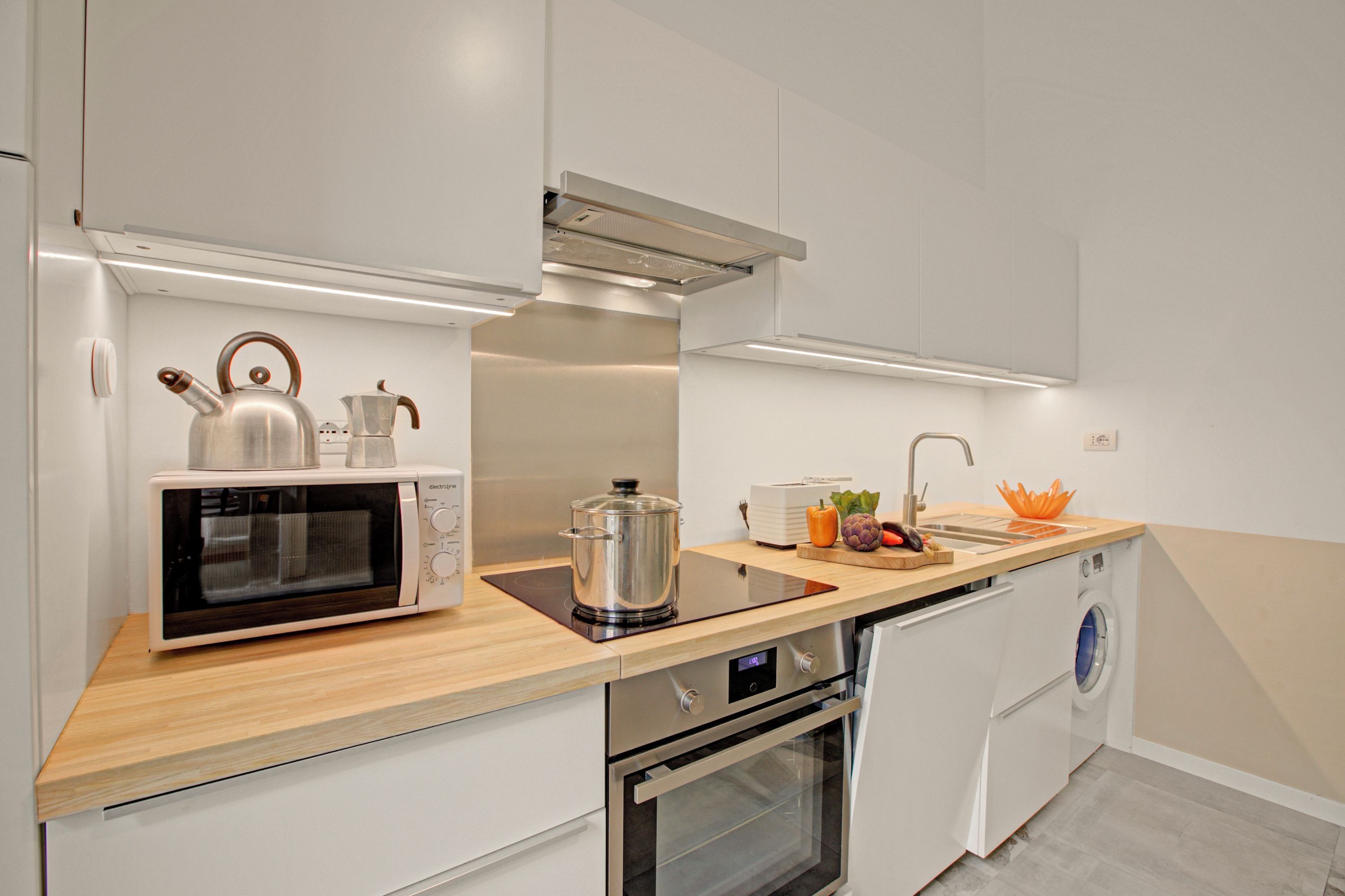 A modern kitchen with a microwave, kettle, induction cooktop, oven, and washing machine.