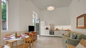 A modern kitchen with white cabinets, a dining area with a round table and chairs, and a green sofa in a spacious living area.