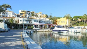 A marina with boats docked, a waterfront promenade, and buildings with commercial establishments. - Penthouse @ Las Mimosas Cabopino (Marbella)