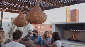 Een groep mensen dineert buiten bij een restaurant, met een bakstenen muur en een bordje waarop 'MOTEL' staat.