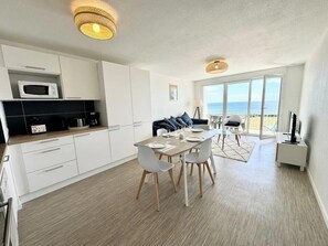 Een moderne keuken met witte kasten, een magnetron en een eethoek met een tafel en stoelen.