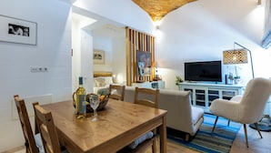 A cozy living room with a wooden dining table, a sofa, and a TV. - Casa da Tammy Olhão Portugal (Olhão)