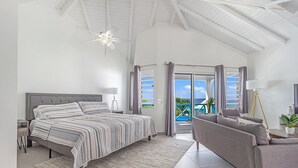 A spacious bedroom with a large bed, a sofa, and a balcony with a view.